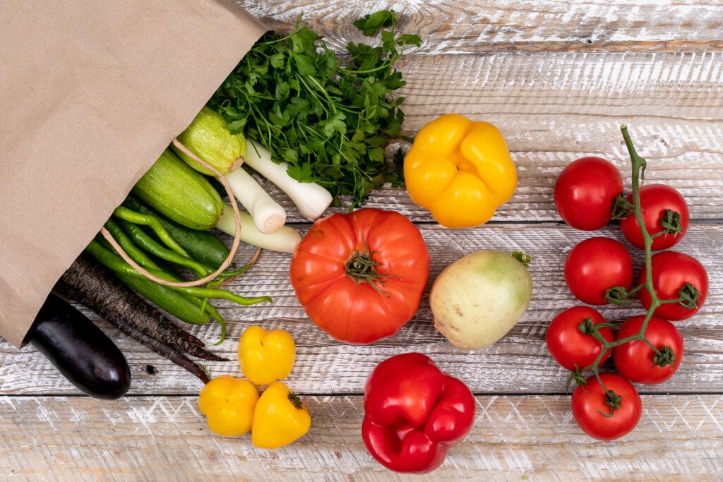 Vegetables shown spilling onto a table from a paper bag.