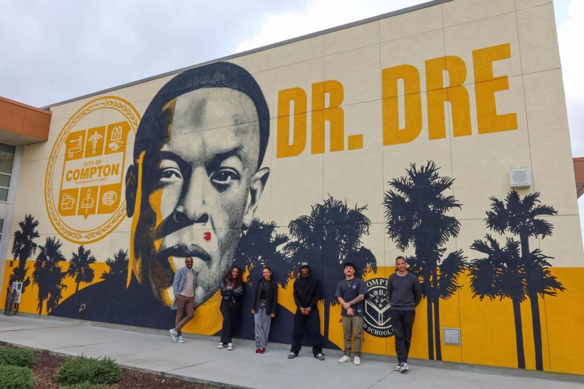 AEG team members pose outside Compton High School in front of the Andre “Dr. Dre” Young Performing Arts Center mural during a campus visit focused on career exposure and community engagement.