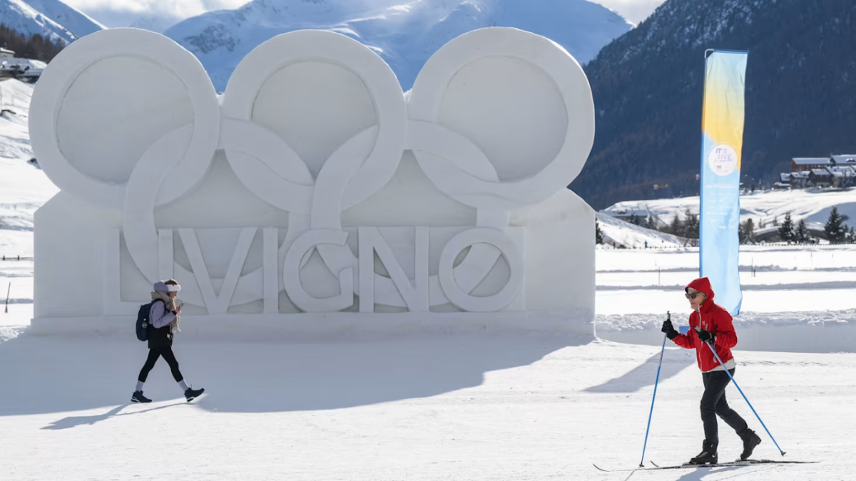 People skiing past Livigno Olympic snow sculpture