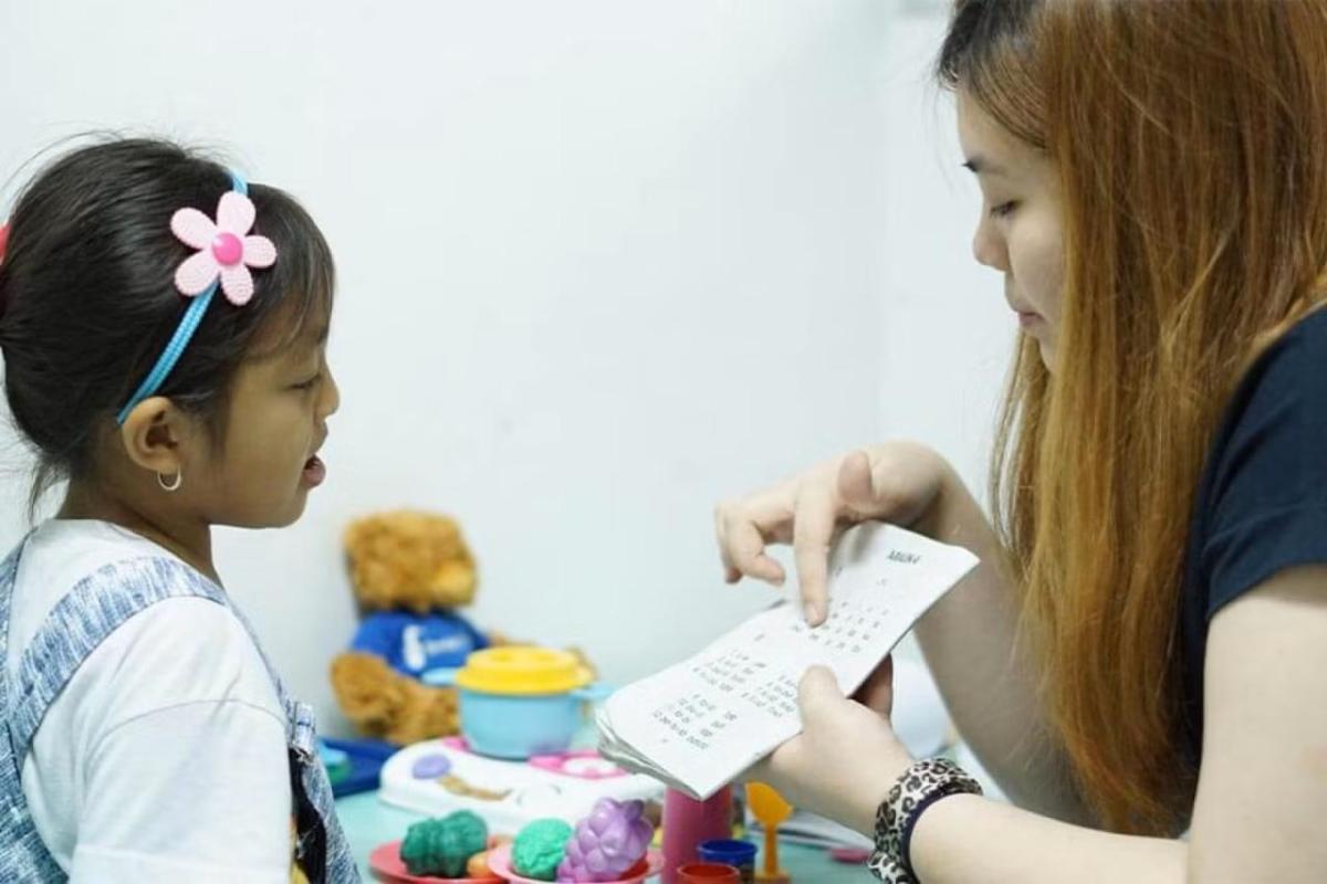 A caregiver works one-on-one with a young child during a speech therapy session.