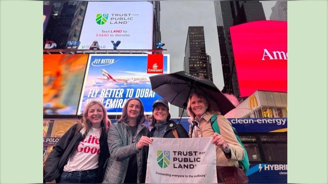 Four people together, holding up a sign that says "Trust for Public Land"