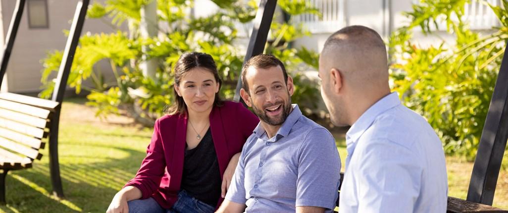 Three people talking, seated on a park bench