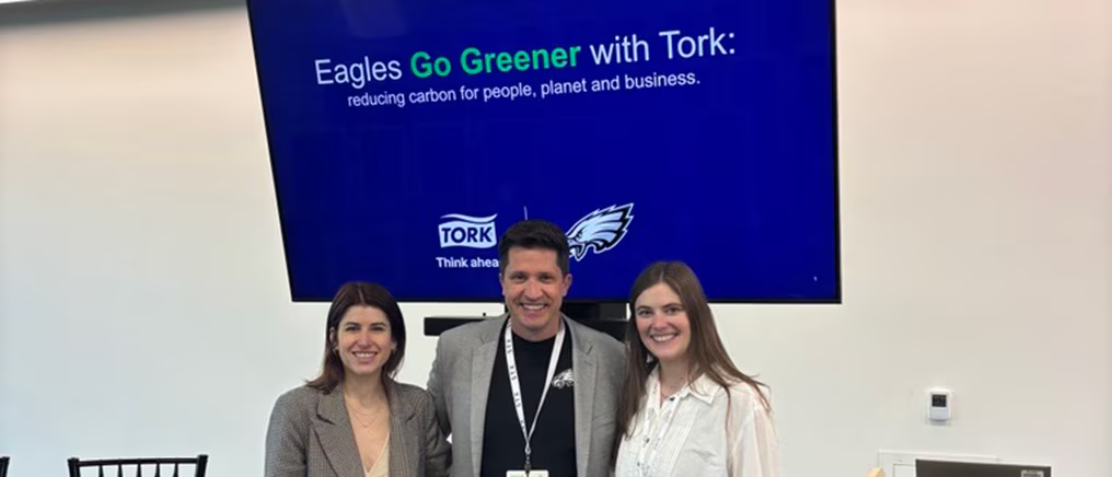 Three people standing in front of presentation. Screen behind says, "Eagles Go Greener with Tork"