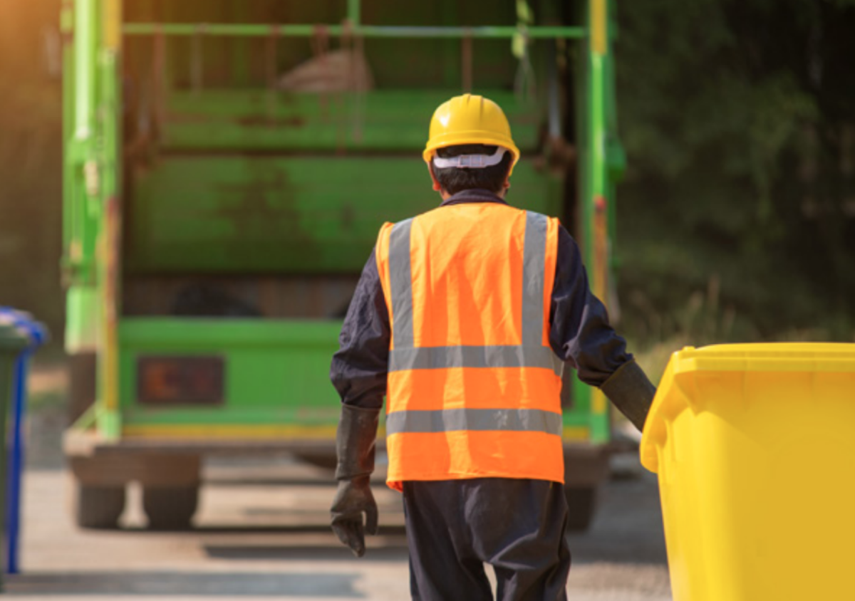A person bringing a yellow garbage bin towards a garbage truck.