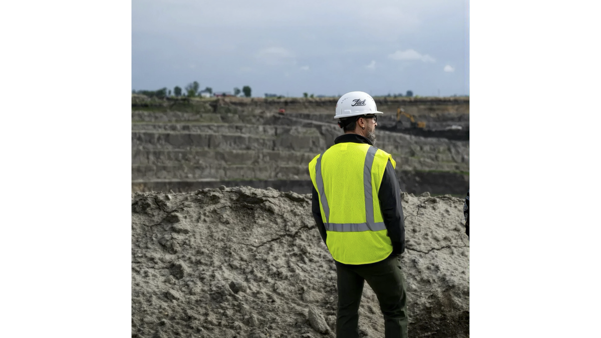 Man in hard hat and yellow vest looking out over mining site
