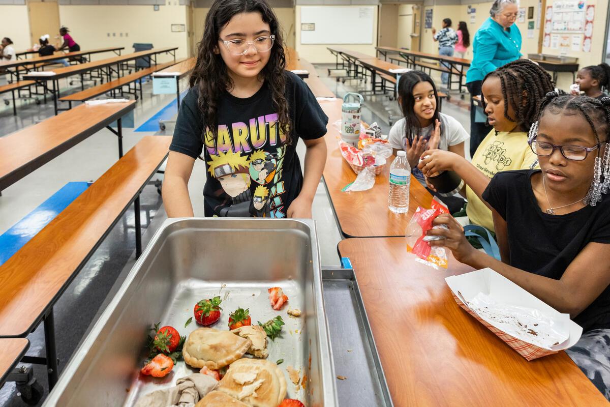 A student pushes a cart to collect food waste from fellow students in a school cafeteria.