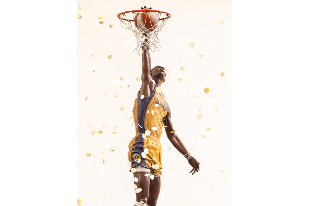 Close-up view of bronze Los Angeles Sparks basketball player Lisa Leslie statue reaching through the hoop as gold confetti falls around it.