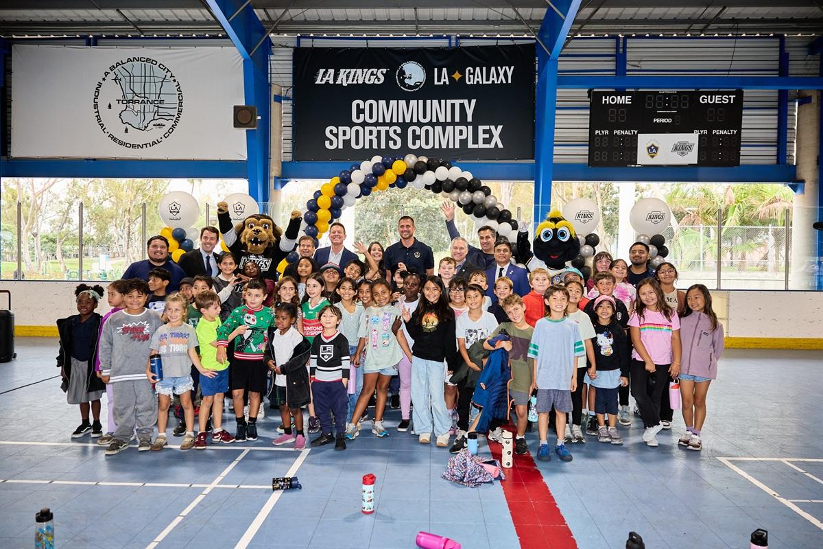 A large group of children and adults pose with the LA Kings and LA Galaxy mascots beneath signage for the LA Kings and LA Galaxy community sports complex in Torrance.