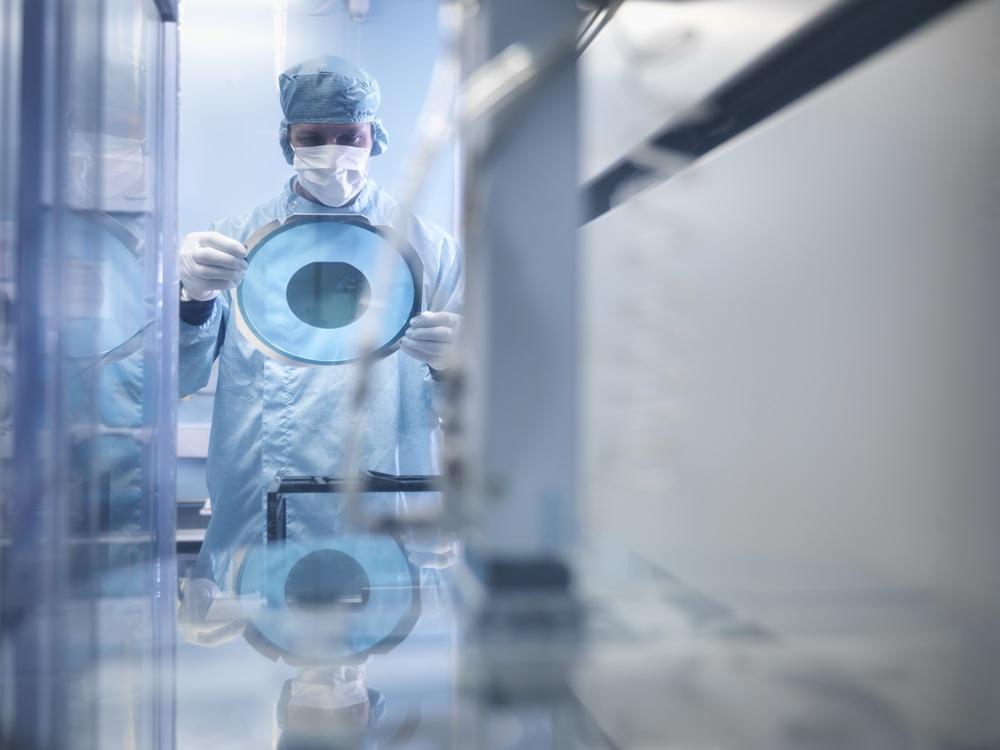 Gowned and gloved technician working on a semiconductor.
