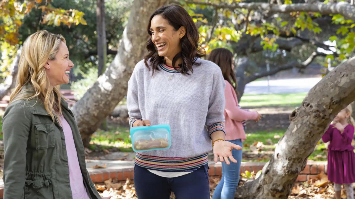 Two women talking outside while children play nearby