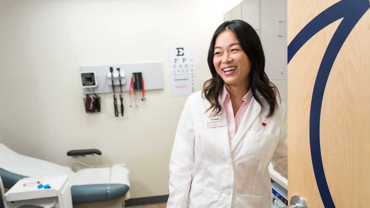 A smiling healthcare worker at the entrance of an exam room