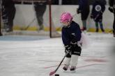Participant in full hockey gear skates on the ice while practicing puck control during LA Kings Girls Camp. A pink helmet and matching hockey stick stand out against the rink background.