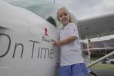 Young girl standing next to plane, pointing at her name (Olivia) printed on it.