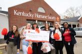Six people standing together outside in front of the Kentucky Human Society, holding a large check