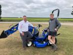 Two people standing in a field next to a blue tractor