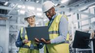 Workers in hard hats and safety vests looking at a laptop