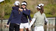 Two golfers hug as a third approaches them. All carrying golf clubs.