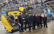 A group of people stood in front of yellow agricultural machinery 