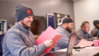 People sitting at a desk with laptops and red folders
