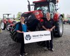 Two people stand in front of a tractor with a "Meet the Need" sign