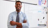 Teacher standing in the front of class with arms crossed, smiling.