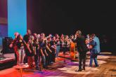 A group of students on stage with a small orchestra and conductor, all the students wearing "Mano Down" t-shirts.
