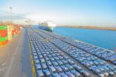 Rows of finished vehicles staged at a port terminal alongside a cargo vessel, illustrating large-scale automotive imports and exports supported by integrated logistics operations.