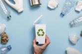 a hand holding a small recycling bin surrounded by plastic bottles