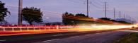 Long exposed lights from a vehicle on a road, power lines along the side of the road.