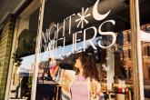 A person cleaning a window of a store called Night Dwellers.