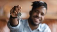 A person of color is holding a key chain with house keys and is smiling.