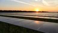Long rows of solar panels, a rising sun inthe distance.
