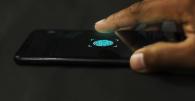 A close-up of a finger poised to tap a fingerprint scanner icon on a smartphone screen, indicating biometric authentication.