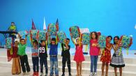 Group of children stood in a line in front of a blue wall holding up matching bags