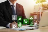 Business employee working at desk with sustainability related symbols in foreground