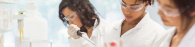 Three people in protective lab gear. One holds a pipette.