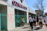 Community volunteers gather on a sidewalk as a KYCC cleanup leader provides instructions in front of a building marked with graffiti.