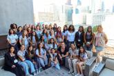 A large group of participants gathers on an outdoor terrace with city buildings in the background, posing together during a group activity.