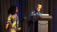 Bridget Ndagaano and Yvette Raphael on stage. Yvette behind a podium with microphone.