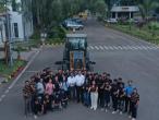 Aerial view of a group of people posed in front of large tractor, each giving 'thumbs-up'.