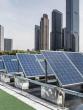 A row of tilted solar panels, a city-scape behind them