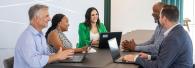Lesly Luque and team at a conference table, some with open laptops.