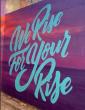 sign reading, "We Rise For Your Rise"