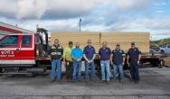 A group of seven people in front of a truck with loads of OSB boards on the trailer.