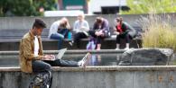 Student sat on a wall using their laptop 
