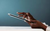 Close-up of a person’s hands using a digital tablet, with fingers gently tapping the screen against a soft blue background.