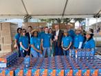 A group of people standing behind a table full of bobbleheads in boxes, pallets of boxes behind them.