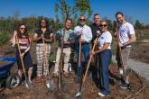 Seven people, including CEO of the Arbor Day Foundation, stand with shovels around newly planted tree. 