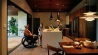 A person in a wheelchair talking with two others at a kitchen island.