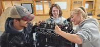 Three smiling people working on a large mechanical piece.
